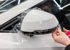 The Process Of Installing Paint Protection Film being applied to car outside mirror.