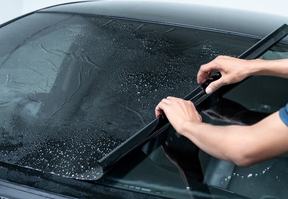 Car window tinting. Male Auto Specialist Worker Hand Rolling Car Window Film On windshield of car.