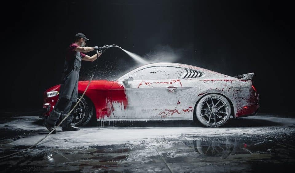 Auto Detailing. Car Wash Expert Using Pressure Washer To Clean A red car.